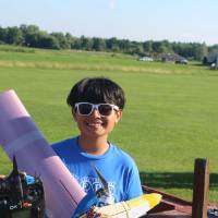 blue team student poses with their plane while wearing sunglasses